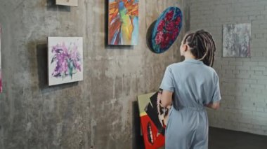 Rastalı genç beyaz bir kadının sanat galerisindeki resimlerin akıllı telefonuyla fotoğraf çekişi.