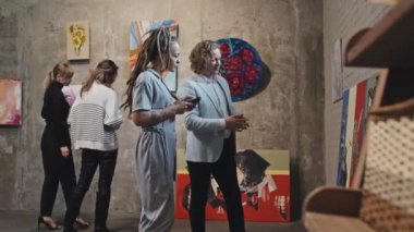 Orta uzunluktaki sarı saçlı Kafkas erkek ve kız Rasta bukleli ve gündüzleri çağdaş sanat galerilerindeki resimlere bakıyorlar.