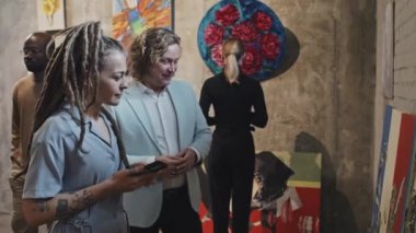 Gündüz vakti çağdaş sanat galerilerinde konuşan ve sanat eserlerine bakan sarı saçlı beyaz erkek ve kız.