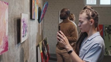 Rastalı beyaz bir kızın resimlerini çekerken gündüz sergilenen resimlerin akıllı telefonuyla gezerken, ziyaretçiler...