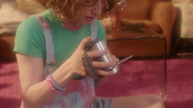 80 'lerin modasında kızıl saçlı beyaz bir kızın gündüz vakti oturma odasında oturup eski moda video kamera kullanması.