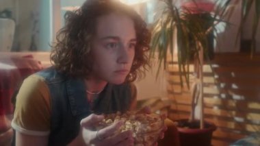 Orta boylu, kızıl saçlı, beyaz bir kız, 80 'ler tarzında iç tasarımı olan bir odada oturuyor, korku filmi izliyor ve patlamış mısır yiyor, korktuğunda saçıyor.
