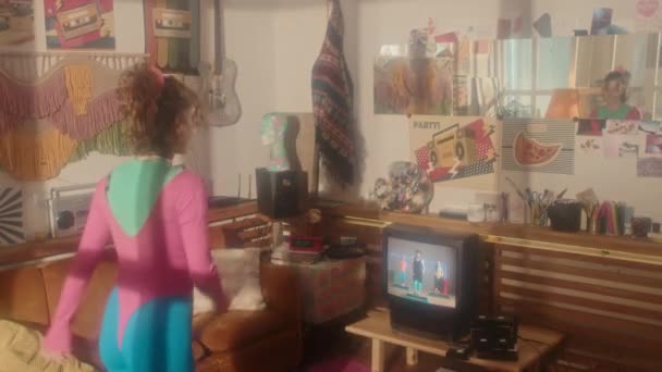 80代の若い赤髪の女の子の後部ビュー有酸素運動でフィットネステープで午後のリビングルームでレトロなテレビで実行 — ストック動画