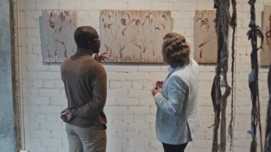 Sarışın, beyaz bir adam ve genç Afrikalı Amerikalı arkadaşının modern sanat galerisinde gündüz resimleri tartışırken orta boy dikiz manzarası.