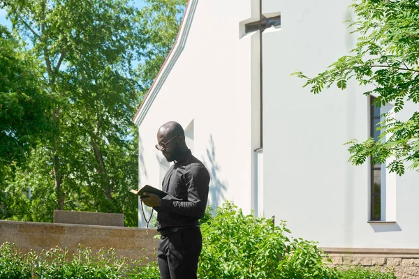 Вид Сбоку Молодого Проповедника Черной Одежде Смотрящего Открытую Священную Библию — стоковое фото