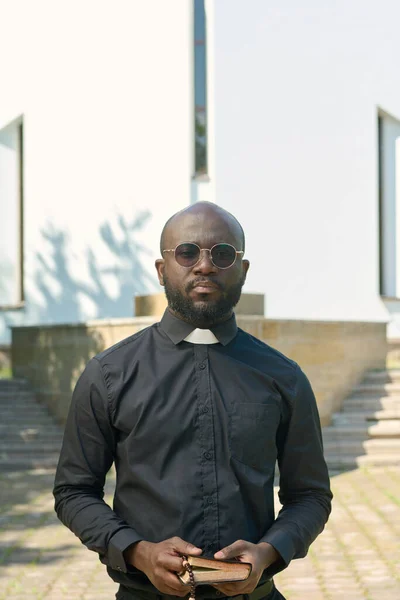 年轻而严肃的牧师 身穿黑色衬衫 头领着 在教堂前祈祷或宣讲教义 — 图库照片