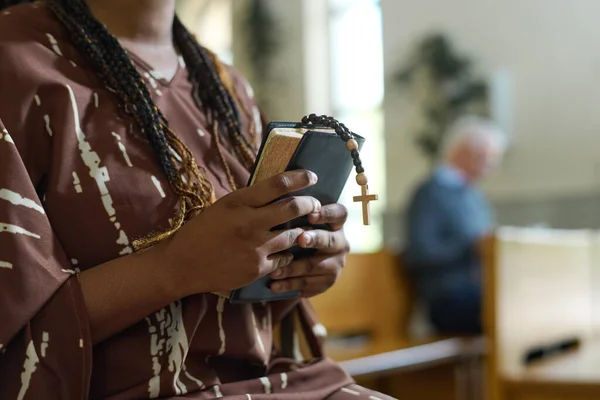 聖書を持つ若い黒人女性の手と教会に立って説教の後に祈る小さな木製の十字架とバラ色のビーズ — ストック写真