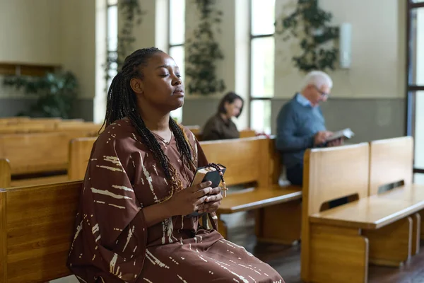 年轻的基督教黑人妇女穿着休闲装 坐在教堂的长椅上向上帝祈祷 眼睛紧闭着 — 图库照片