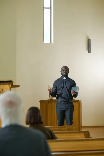 カトリック教会の説教壇に立ちながら 教区の人たちとコミュニケーションを取る聖職者の服を着た若いアフリカ系アメリカ人聖職者 — ストック写真