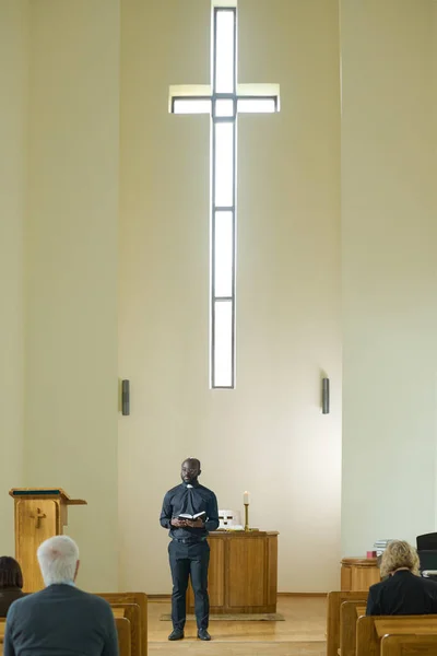 Афроамериканський Священик Чорному Вбранні Проповідує Парафіянам Стоячи Навпроти Кафедри Стіни — стокове фото