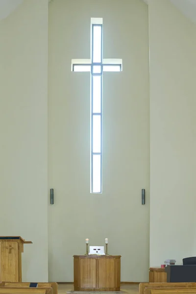 Empty service hall in modern catholic or evangelical church with cross on wall above wooden pulpit with altar and two candles
