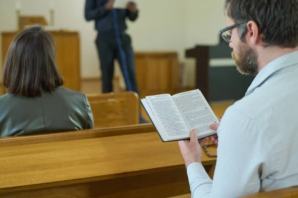聖書を開いている中年の男性は 机のそばに座って教会の礼拝中に説教を聞きながら 福音からの聖句を読んでいます — ストック写真