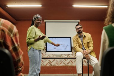 Genç Afrika kökenli Amerikalı konuşmacı, meslektaşlarına açıklarken bilgisayar ekranına diyagramlar ve diğer finansal verilerle işaret ediyor.