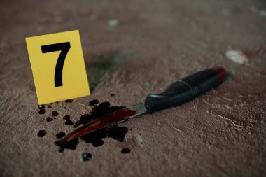 Cinayet silahını temsil eden bıçağın yakın çekimi. Cinayetin işlendiği yerde suçlunun bıraktığı asfaltta ölü kurbanın kan lekeleri var.