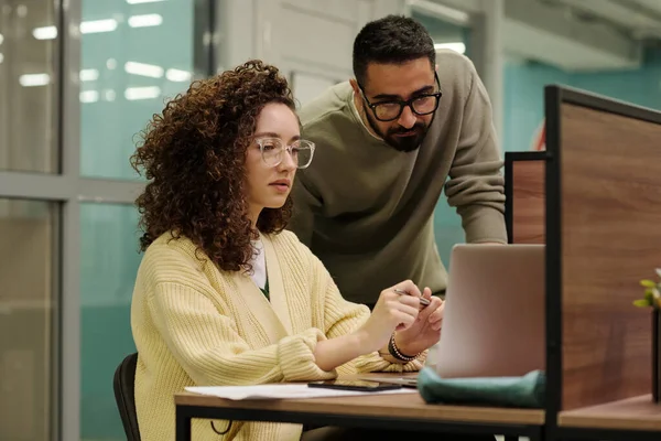 在办公室工作会议上 两名戴眼镜和便衣的年轻同事在笔记本电脑屏幕上浏览数据 — 图库照片