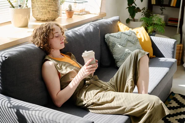 リビングルームで快適なソファに座ってコーヒーを飲みながら仕事のアイデアを考えている — ストック写真