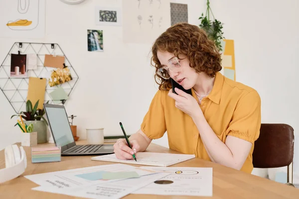 Joven Freelancer Consultando Clientes Teléfono Móvil Tomando Notas Papel Mientras — Foto de Stock