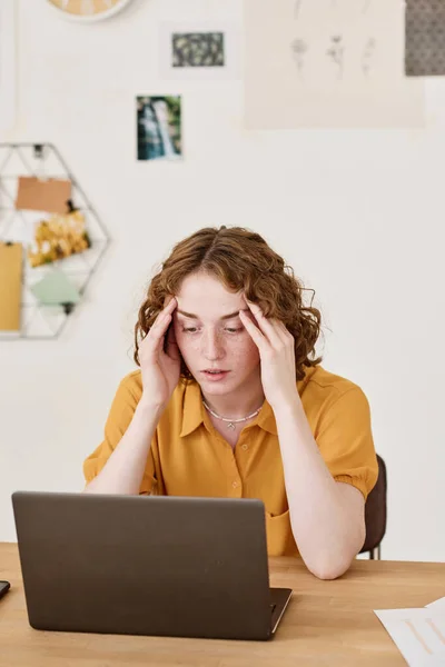 年轻的女商人坐在笔记本电脑前的桌子旁 浏览在线数据时 表现出误解或疲倦 — 图库照片