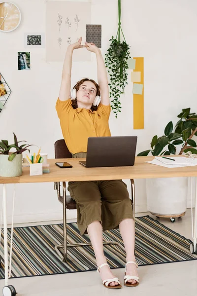 年轻疲惫的女性自由职业者或设计师在工作场所的笔记本电脑前伸出手来放松自己或思考新的想法 — 图库照片
