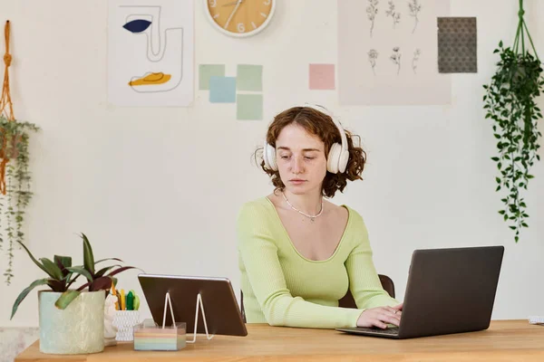 坐在笔记本电脑前 打字和看平板电脑屏幕时 认真学习耳机联网的年轻女商人或女学生 — 图库照片