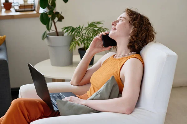 快乐的年轻女商人或家庭办公室经理 带着笔记本电脑坐在舒适的扶手椅上 用手机说话 — 图库照片