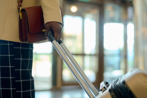 ホテルのラウンジを歩いている間に荷物でスーツケースを引くハンドバッグスマートカジュアルで若い黒人女性の手 — ストック写真