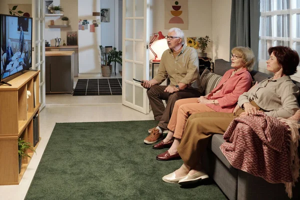 三位老朋友坐在电视前舒适的沙发上 坐在宽敞的客厅里观看他们最喜欢的系列片 — 图库照片