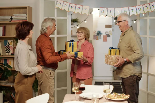 两个年长的男人带着许多生日礼物祝贺聚会上快乐的老年妇女 她们站在桌旁享用自制食物 — 图库照片