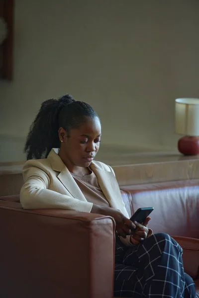年轻优雅的黑衣女子穿着正装 用智能手机发短信 或在宾馆房间沙发上放松时用视频聊天 — 图库照片