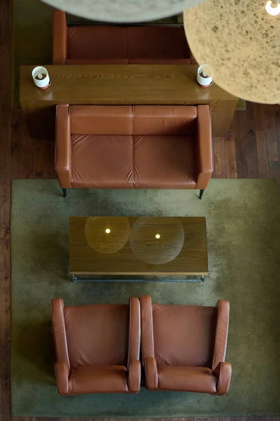 酒店客房灰色地毯上的棕色皮革沙发和围绕矩形木制桌子的两张扶手椅的上方 — 图库照片