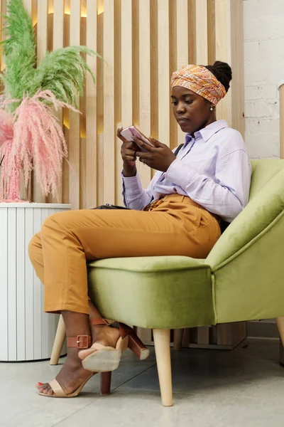精品美容院或美容院的年轻非洲裔美国女性顾客坐在舒适的扶手椅上 用手机发短信 — 图库照片