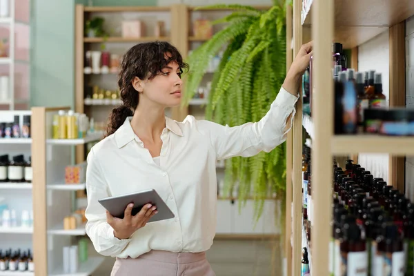 Jonge Vrouwelijke Winkelassistent Met Tablet Voor Het Display Met Verschillende — Stockfoto