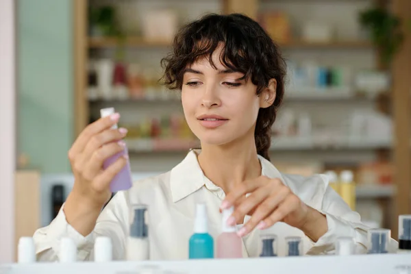 化妆品超级市场的年轻女性员工在小塑料瓶中翻阅各种新的美容产品 — 图库照片