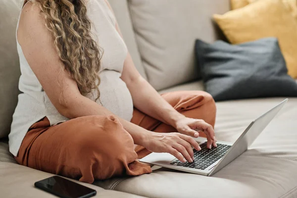 年轻孕妇坐在手提电脑键盘上打字 双腿交叉坐在客厅沙发上和上网的剪影 — 图库照片