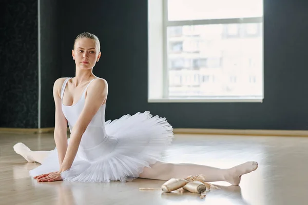 年轻漂亮的芭蕾舞蹈演员穿着白色的燕尾服 坐在一边 双手挽着身体 保持平衡 — 图库照片