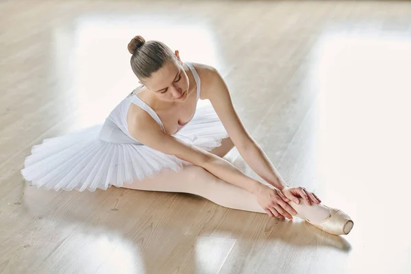 年轻的芭蕾舞蹈演员穿着白色的燕尾服 在复读时弯着腰坐在教室的地板上 — 图库照片