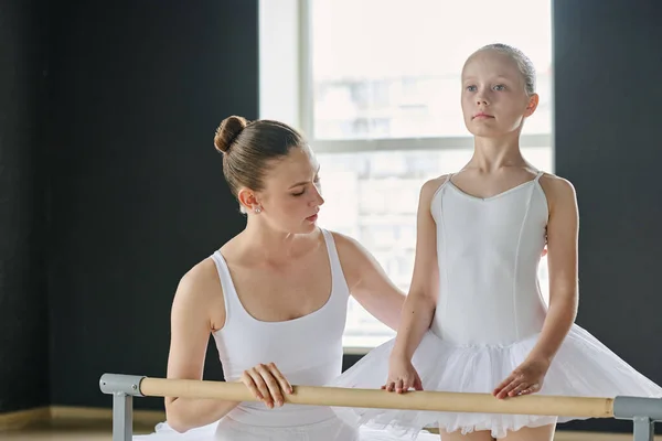 在课堂上 年轻的芭蕾舞导师站在身穿白衣的年轻学习者一边 帮助她进行舞蹈练习 — 图库照片