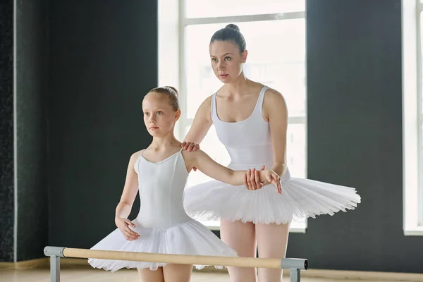 若いバレエのインストラクターは 白いチュチュで若い女の子の腕を保持しながら 彼女のパフォーマンス中にバランスを保つ方法を説明します — ストック写真