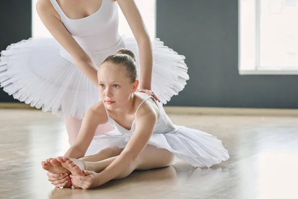 年轻的女孩一边努力 一边弯腰伸腿 而年轻的芭蕾舞教练在练习时帮助她 — 图库照片