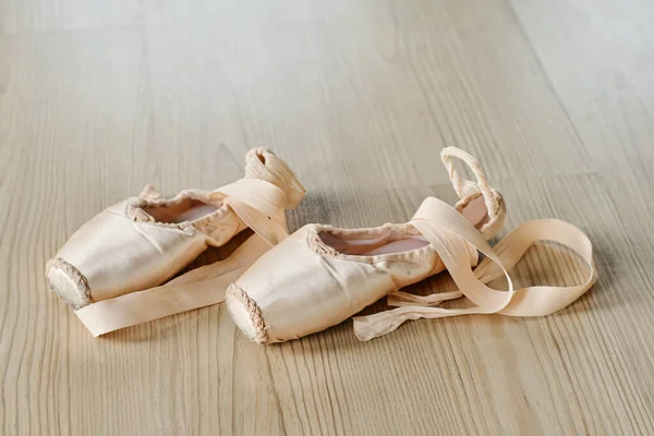 Pair of new untied pointe shoes of beige color with silk ribbons on the floor of dance hall or classroom for repetitions of ballet exercises
