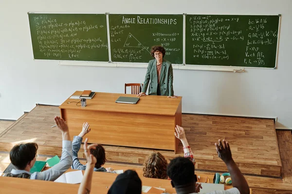 一群不同种族的学生举手向站在黑板旁的老师提问 他们有公式和方程式 — 图库照片