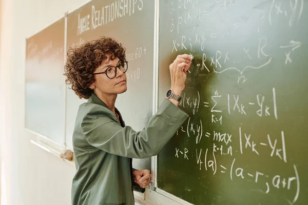 Σοβαρή Γυναίκα Δασκάλα Της Άλγεβρας Κιμωλία Γράφει Εξισώσεις Στον Πίνακα — Φωτογραφία Αρχείου