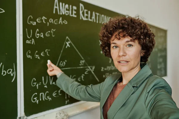 在向网上听众讲解时 穿着正装的自信几何老师用公式和三角形指着黑板 — 图库照片