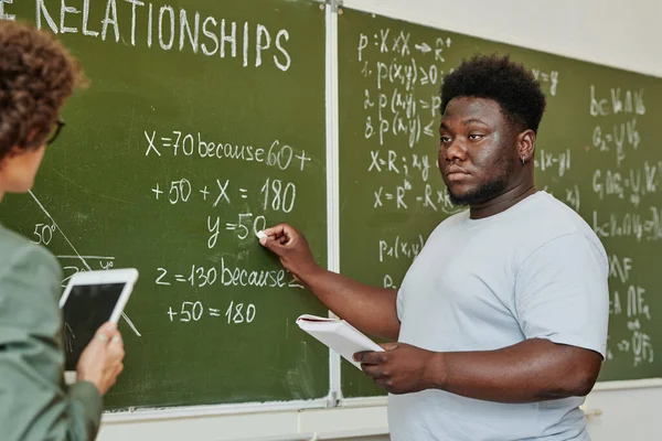 在解释方程或定理的过程中 年轻的非裔美国学生指着黑板 看着老师 — 图库照片