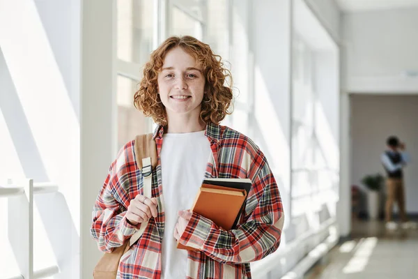 快乐的年轻学生穿着便服 拿着书本和背包 在休息的时候站在学校走廊里看着相机 — 图库照片