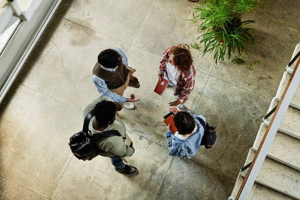 階段のそばに立っている間 授業の合間に大学の廊下で話をしている大学の10代の学生4人のショットの上に — ストック写真