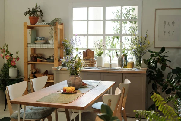 台所用品や窓や緑の国内植物による野草とシンクに囲まれた中心部に木製のテーブルと居心地の良いキッチン — ストック写真
