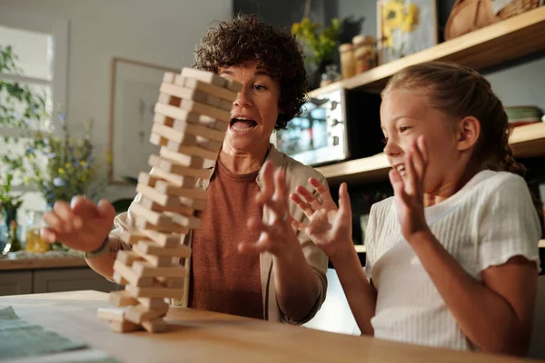 年轻女子和她年幼的女儿在比赛中坐在桌旁 试图抓住倒塌的塔楼 塔楼是用木块建成的 — 图库照片