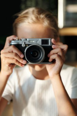 Genç sarışın kızın elleri yüzüne retro fotoğraf makinesi tutarken natürmort çekerken ya da önünde dikilen insanları çekiyor.