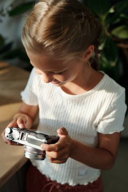Beyaz tişörtlü meraklı genç kız boş zamanlarında eğlenirken eski fotoğraf makinesinin ekranında yeni fotoğraflara bakıyor.